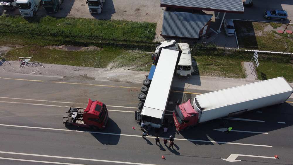 Aerial view of a road accident involving two large trucks on a highway. One truck is overturned, the other is parked in front.