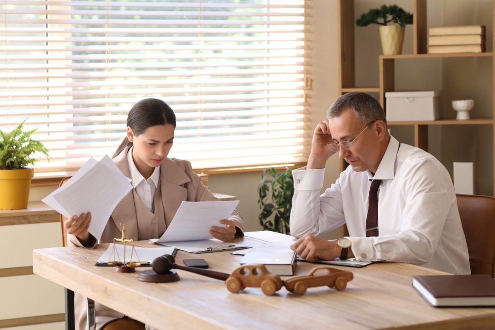 A man and woman in formal attire review documents at a wooden desk