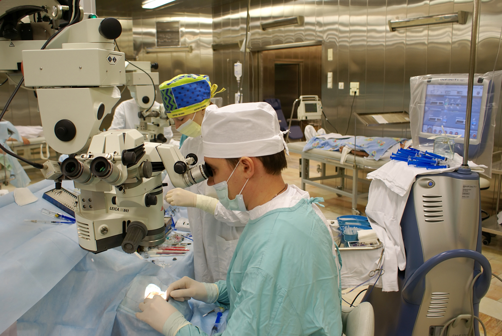 Surgeons using a microscope during a medical device implantation procedure in an operating room.