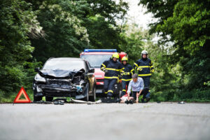 Emergency responders assisting an injured person after a serious car accident on a rural road.